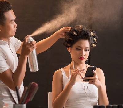 Mujer en un salón de belleza utilizando celular un estilista realiza su trabajo